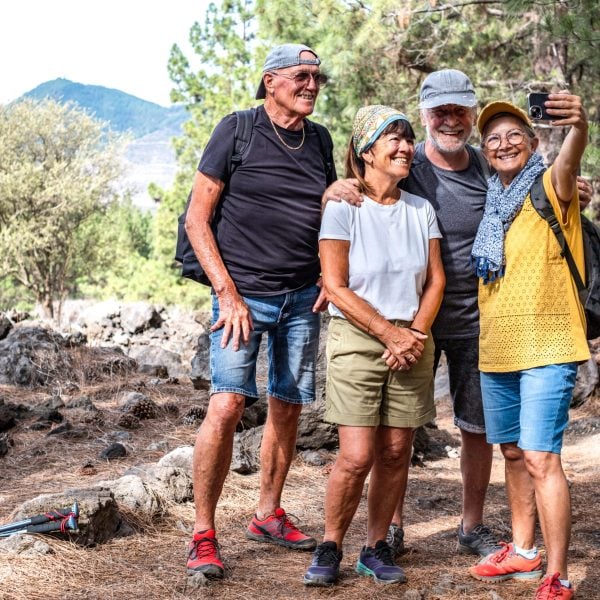 Happy group of senior friends enjoying retirement and adventure trekking in the forest, four elderly people take a selfie smiling. Sport, freedom, healthy lifestyle concept